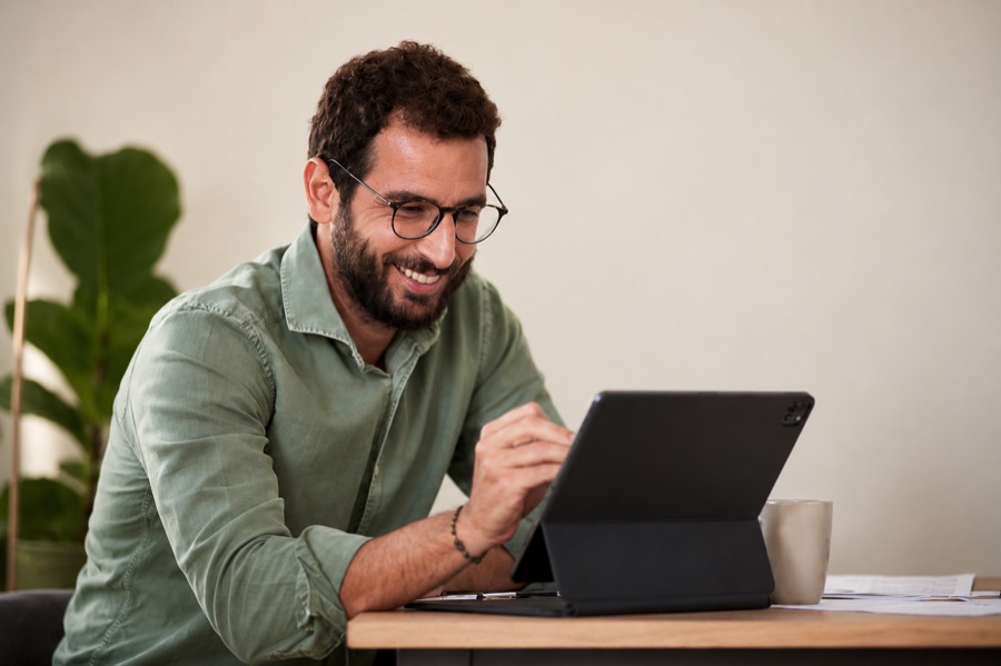 Homem sorrindo enquanto trabalha num tablet sobre a mesa
